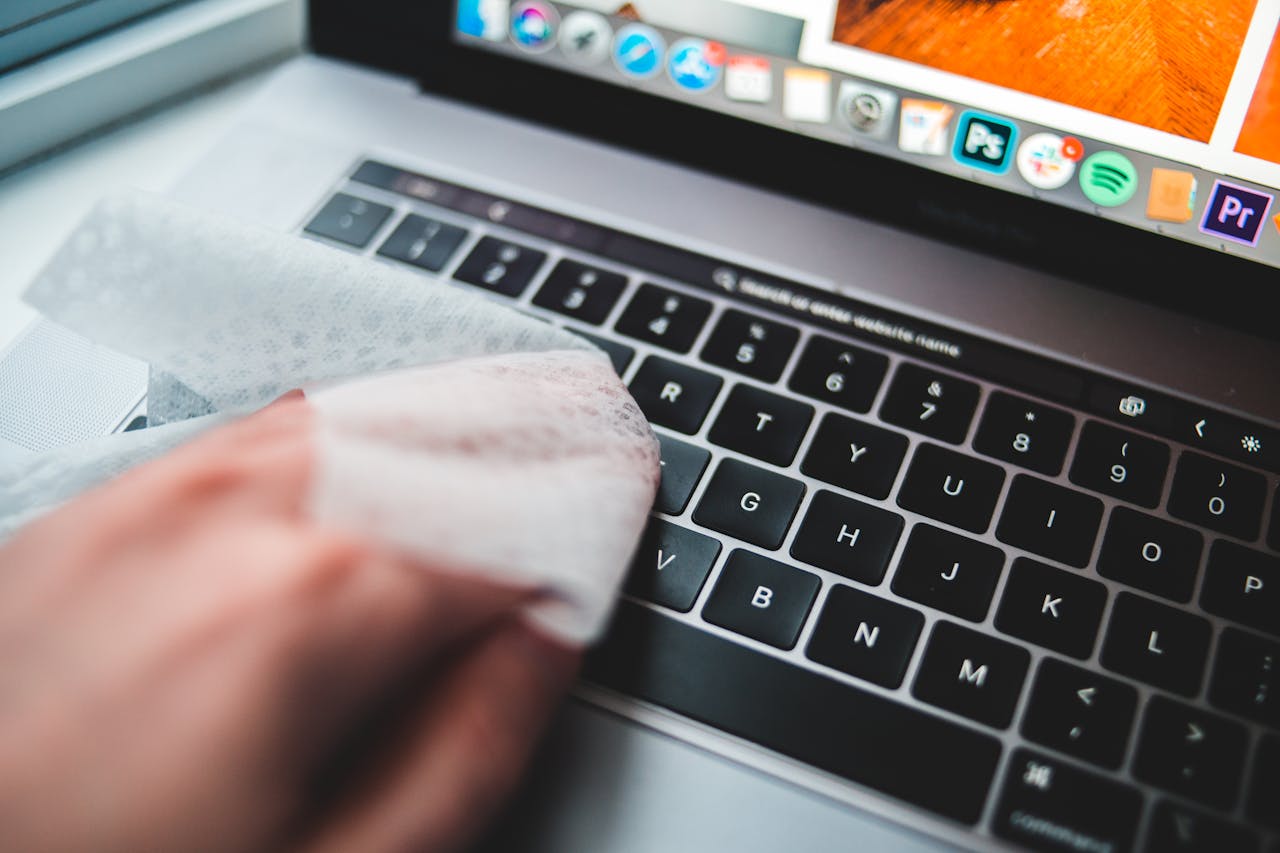 Person cleaning a laptop keyboard using disinfectant wipes for hygiene.